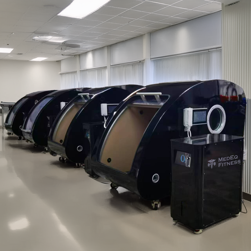 Row of black capsule-style fitness machines in a room with white walls and tiled floor.